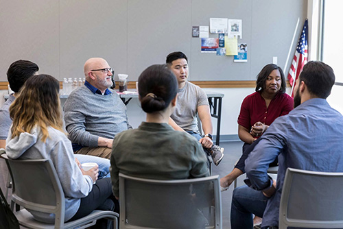 A group of people of all ages sit on chairs in a circle and talk