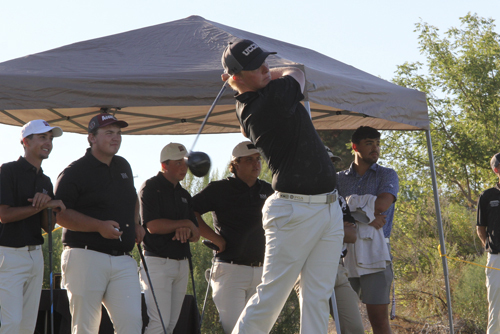 A UCCS student swings a golf club at an outdoor event.