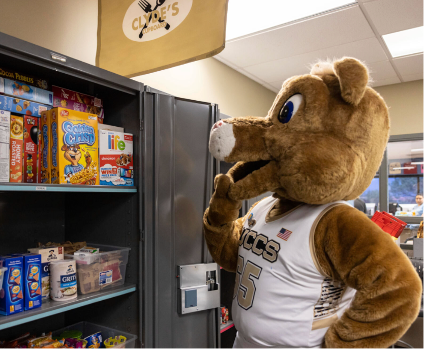 Clyde mascot standing in front of food shelves