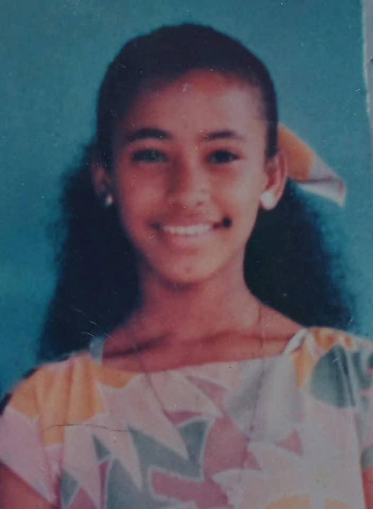 Salwa Bamba as a teenager, she is smiling and wearing a white dress with pink, green and yellow geometric designs.