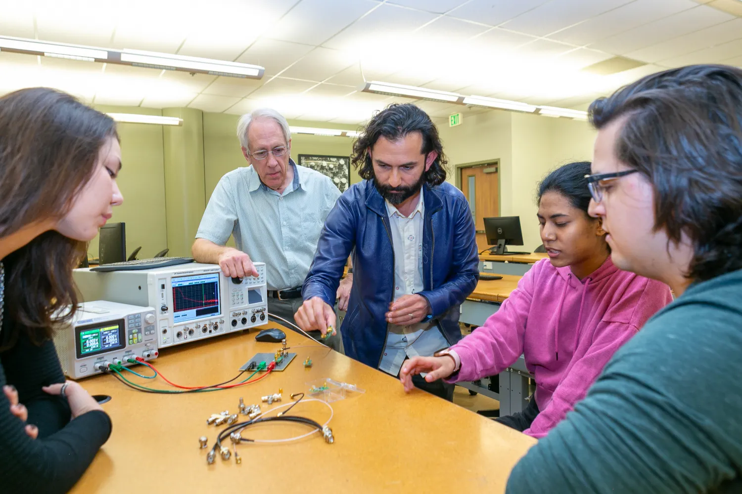 Students and faculty stand around a table looking at computer hardware